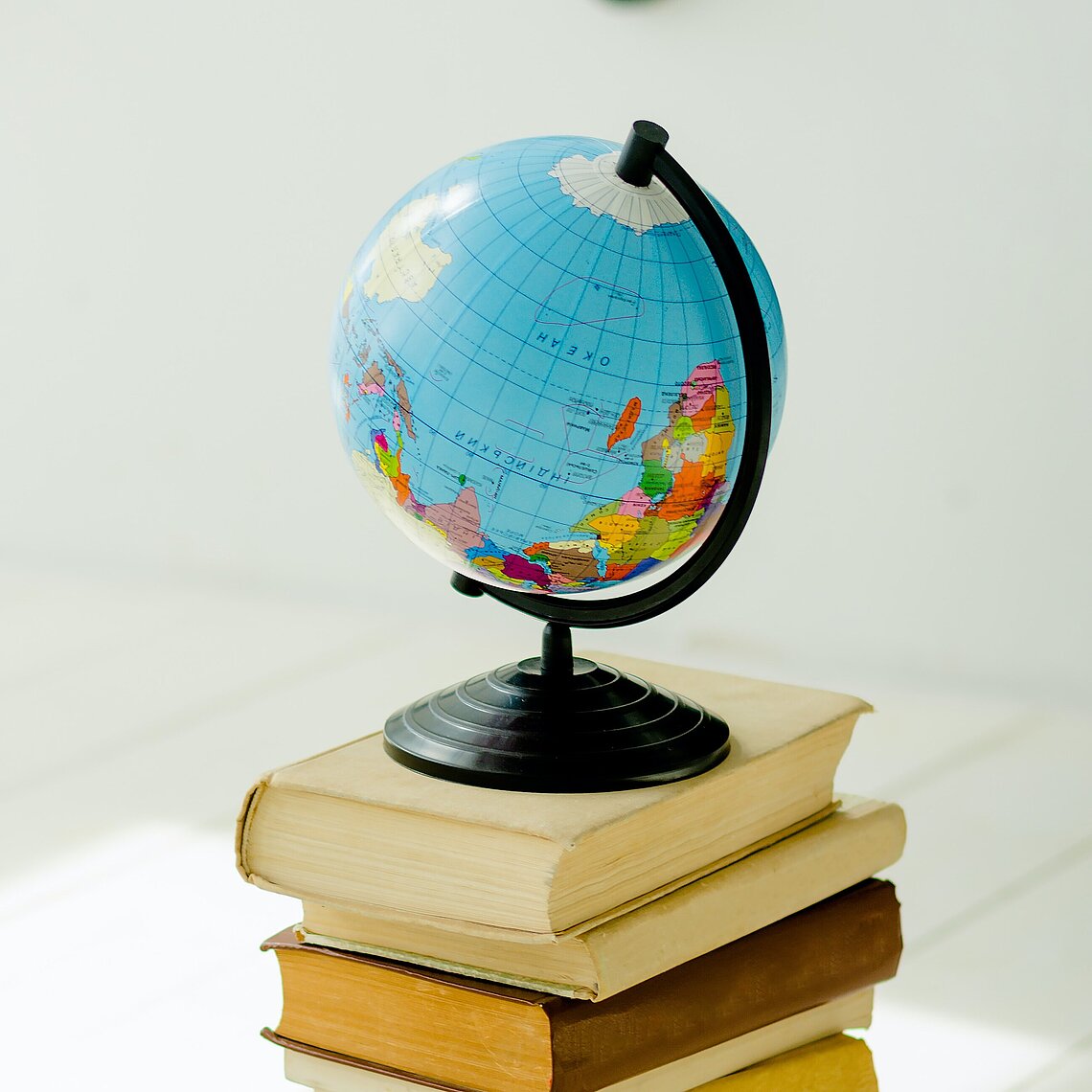 Ein kleiner Globus steht auf einem Stapel mehrerer Bücher auf einem hellen Holzboden.