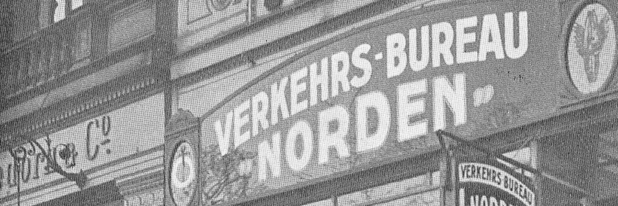 Schwarz-weiße Außenaufnahme einer Ladenfront mit dem Schild 'VERKEHRS-BUREAU NORDEN' und weiteren kleineren Schildern.